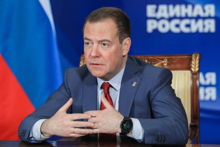 Dmitry Medvedev seduto su una sedia a un tavolo davanti a uno sfondo scritto in russo.
