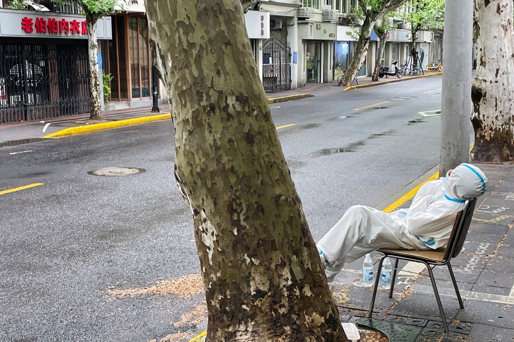 Un operatore sanitario stanco siede lungo una strada vuota a Shanghai, in Cina.