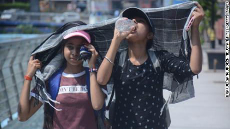 Le ragazze si coprono la testa mentre camminano e bevono acqua nel caldo torrido pomeridiano di Mumbai.