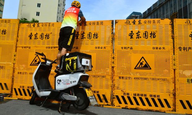 Un corriere in piedi su una bicicletta elettrica per consegnare merci attraverso un posto di blocco a Sanya, nella provincia di Hainan