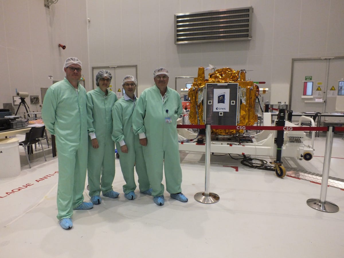 Quattro scienziati, vestiti con abiti verdi e retine per capelli, stanno accanto a un dispositivo delle dimensioni di un forno avvolto in una lamina d'oro.
