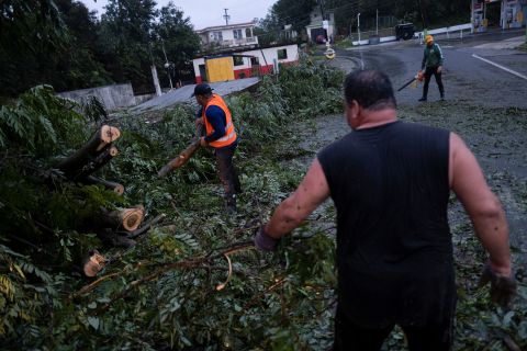 La gente libera un sentiero da un albero caduto a Yaoco, Porto Rico, domenica.